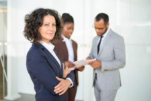 Successful female professional under control smiling at camera while work gets done in background