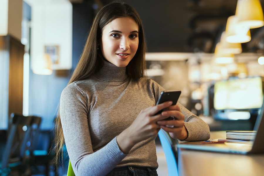 Business woman sitting at table with phone in hand laptop open smiling at camera